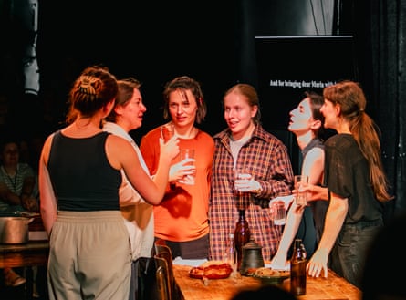 Six members of the all-female cast gather around a table; they are in modern, casual clothing