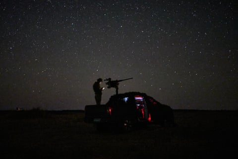 A member of the Ukrainian armed forces looks at a device next to heavy weaponry on the back of a pickup vehicle below a star-filled sky