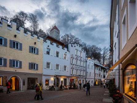 A pedestrianised town street with pastel coloured buildings with shutters and shops with Christmas trees outside