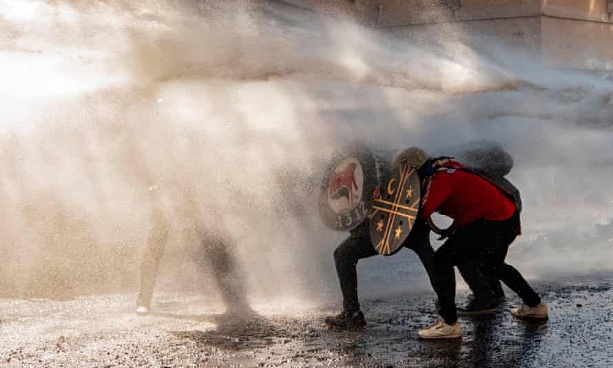 Demonstrators use shields to protect themselves from water sprayed by riot police during clashes on the commemoration of the first anniversary of the social uprising in Chile, in Santiago, on 18 October.