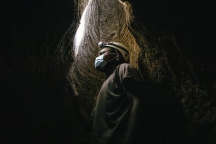 An African man in a hard hat, headtorch and face mask standing in a rock ‘chimney’ in a cave