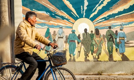 A man cycling past a large mural.