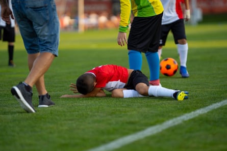 A tackled child lies upset and in pain on the football pitch