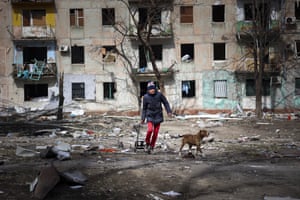 A man walks with his dog near an apartment building damaged by shelling from fighting on the outskirts of Mariupol, Ukraine.