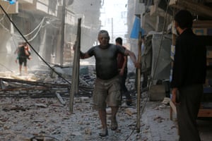 A man covered with dust carries debris down a rubble-filled street
