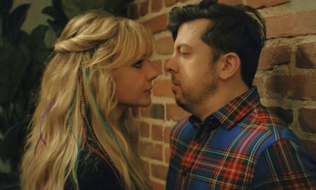 film still of blonde woman and man in checked shirt standing close together looking at each other