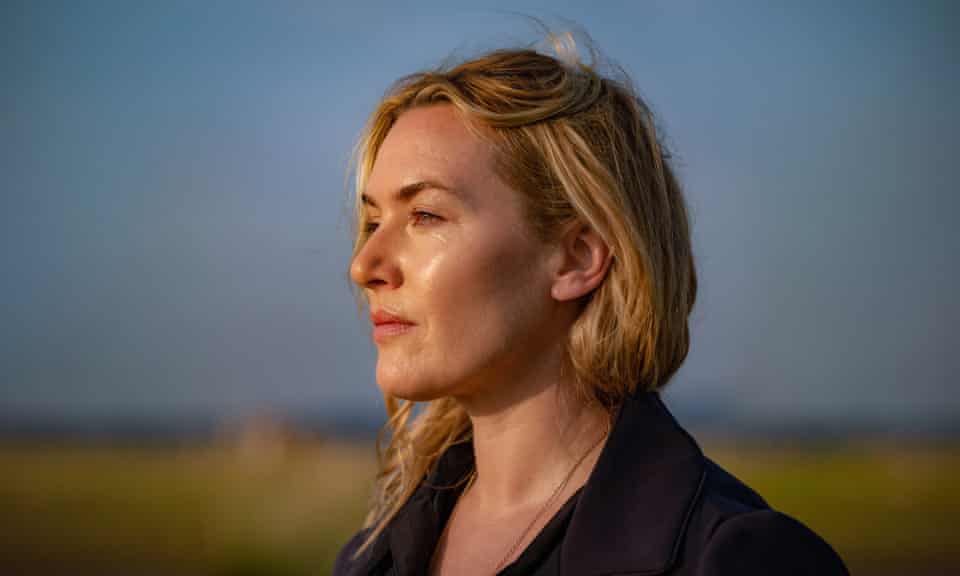Kate Winslet staring out to sea in a blue coat