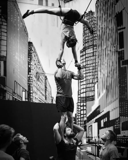 A woman does a handstand split on top of a man who is standing on another man's shoulders