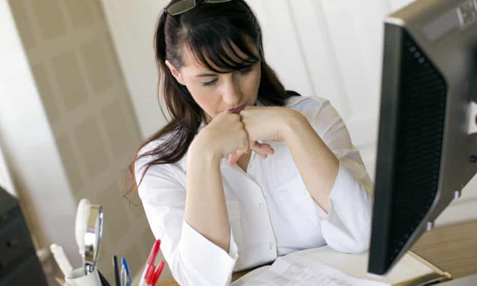 Woman at desk in office with head resting on hands.