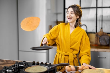 Happy woman cooks pancakes for breakfast, having fun throwing up fried pancakes on the kitchen.