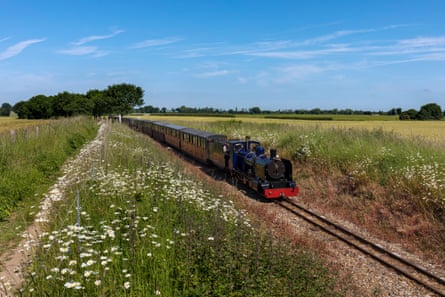 Miniature steam train on single track and path through flat rural landscape