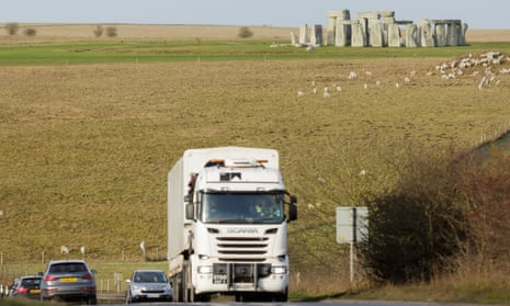 Trucks and traffic pass near by Stonehenge.