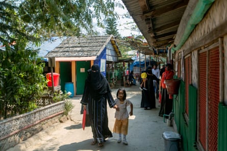 A woman in a burqa walks down a street holding hands with a young gir.