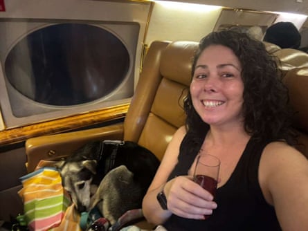 A woman in an airplane holding a glass, taking a selfie.