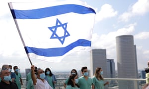 A member of an Israeli Medical team, wearing a face mask, waves a nation flag as the Israeli Air Force (IAF) aerobatic team (unseen) flies in formation over the Tel Aviv Sourasky Medical Center (Ichilov Hospital) during Israel’s Independence Day.