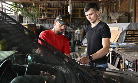 UKRAINE-RUSSIA-CONFLICT-WAR-BLACKSMITHBlacksmith Anton Zaika (R), 32, and mechanic Roman, 39, speak near a car as they work to add windows metal grills in the workshop in Sumy on August 1, 2022. - Anton Zaika, a talented blacksmith artisan who had carved out a modest but successful business selling metal furniture to wealthy European clients, is helping Ukraine’s war effort in his own unique way. When the came five months ago it changed his priorities. Now he makes anti-tank barriers to protect the local volunteer battalion in the northwestern frontline city of Sumy, and special iron stoves adapted to trenches to keep them warm. (Photo by Genya SAVILOV / AFP) (Photo by GENYA SAVILOV/AFP via Getty Images)