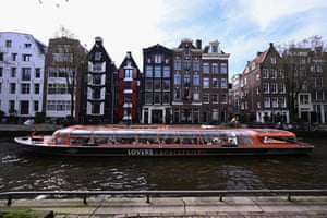 A tourist boat cruises along a canal lined with five-storey buildings