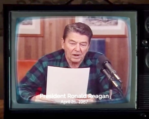 Ronald Reagan, in a blue-and-green checked flannel shirt, reading from a piece of paper into a microphone in a wood-paneled office. dqxikeidqkikdinv