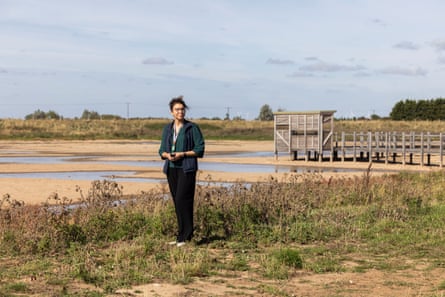 A woman with dark hair and glasses standing in front of a bird watching hut