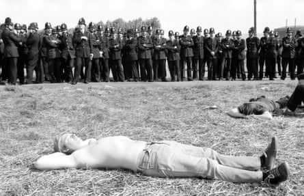 Miners lying on the grass with a line of police officers behind