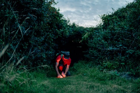 A man crouching down in shrubbery with a small glowing lamp