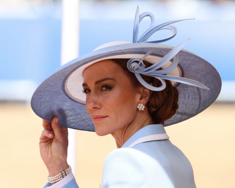 Princess Catherine of Wales in a light blue outfit and wide-brimmed hat looks back over her shoulder