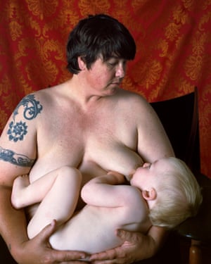Catherine Opie sitting naked on a chair and nursing her son in front of a red backdrop
