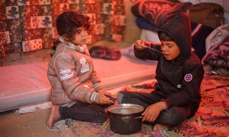Displaced children eat food in Rafah, Gaza.