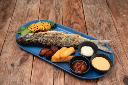 A whole cooked fish on a plate with three small bowls of sauces 