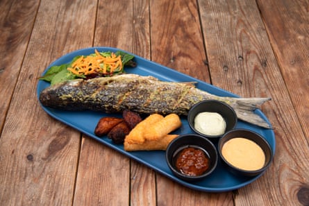 A whole cooked fish on a plate with three small bowls of dips