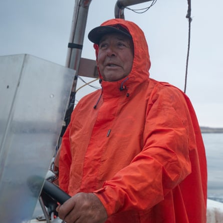 A man in a bright orange waterproof coat steers a boat