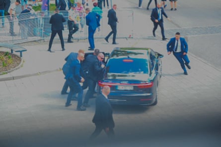 Security officers in dark suits gathered around a car