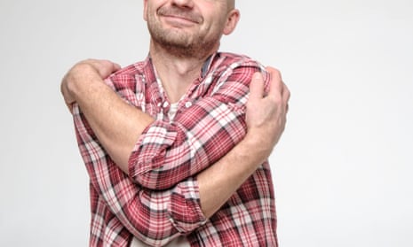 Man in a plaid shirt hugs himself 