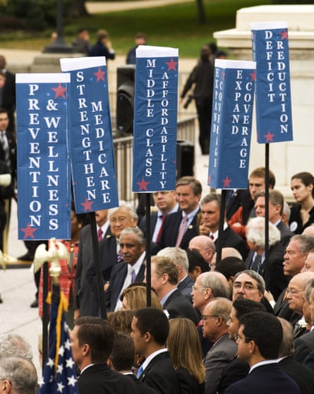 A group of men in suits and some women holding vertical blue and white signs.
