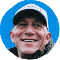 man in baseball cap smiling and looking to side on blue background