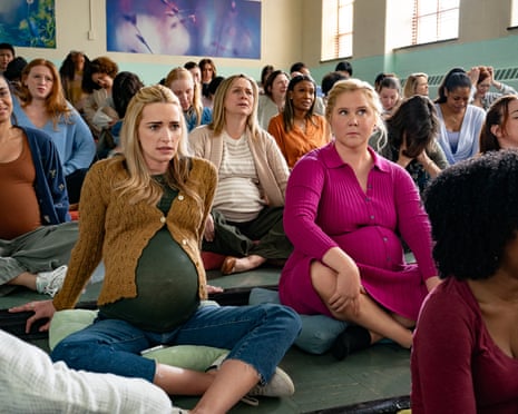 two women sit on cushions in crowd with other people