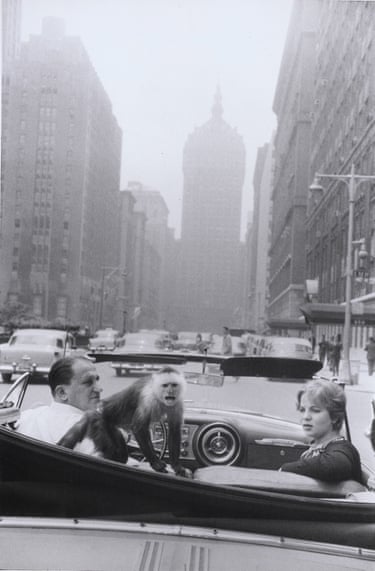 a man and a woman look back at the camera from an open-topped car on Park Avenue with a monkey crouched between them