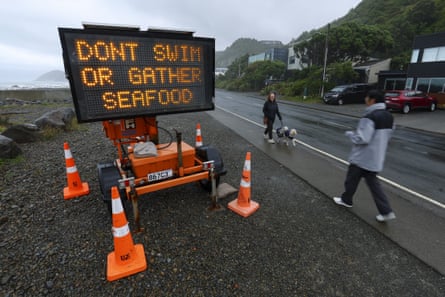 Pedestrians walk past a warning sign between Island Bay and Owhiro Bay.