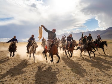 a large group of men on horseback gallop across a sandy valley on horseback