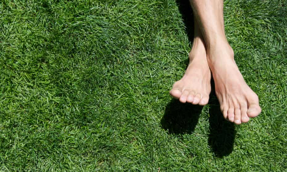 Man's bare feet cross on a patch of bright green grass.