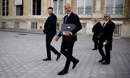 Laurent Wauquiez arrives at the National Assembly in Paris, 9 July 2024: he is walking on a stone plaza in front of a large, grand building with three others. They are all dressed in black suits; Wauquiez is carrying a briefcase under his arm. He is in his late 40s with neat, gelled white hair and trimmed grey beard.