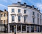 Curved four-storey building rendered in white at top of Deptford High Street.