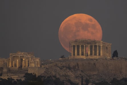 The full moon rises behind the Acropolis hill and the Parthenon temple in Athens on November 8, 2022.