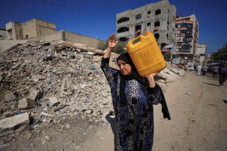 A Palestinian woman carries a water container as she walks past the rubble of a destroyed building in Gaza City.