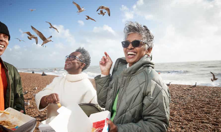 Cheerful male and female friends having french fries at beach on sunny day