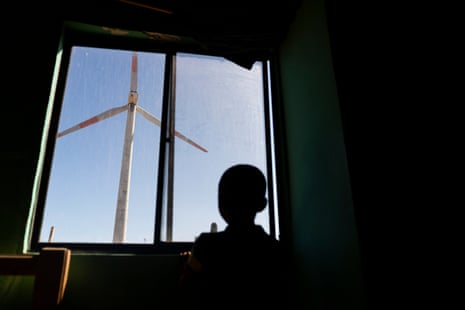 Silhouette of a child looking out of a window in his home at a wind turbine close by with a blue sky as a backdrop
