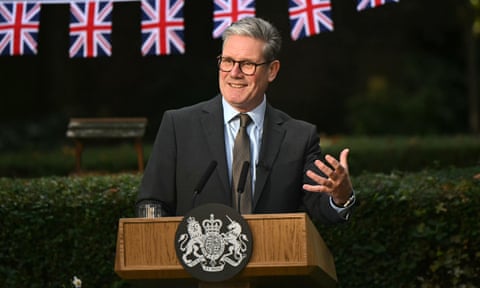 Starmer gestured behind a lectern with small union jack flags in the background