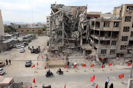 Общий план здания, поврежденного в результате американо-израильского авиаудара, перед которым кто-то разместил фотографии жертв авиаудара на импровизированном мемориале.