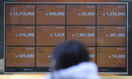 A woman walks by a screen showing prices, including bitcoin, top left, in downtown Seoul, South Korea.