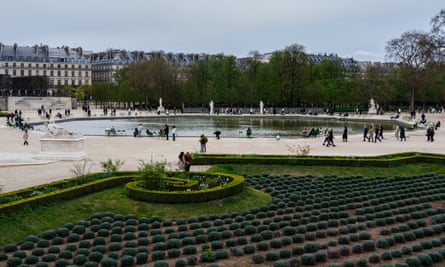 People walking around a pond with a garden in the foreground and multi-storey buildings in the background